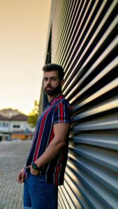 Young male model in a striped shirt posing against a modern building during sunset in Porto, Portugal.